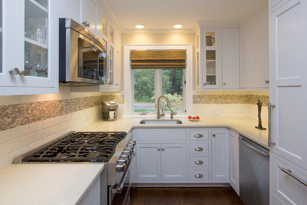 Photo of a small transitional u-shaped eat-in kitchen in Raleigh with an undermount sink, recessed-panel cabinets, white cabinets, quartz benchtops, white splashback, subway tile splashback, stainless steel appliances, dark hardwood floors, no island, brown floor and beige benchtop.
