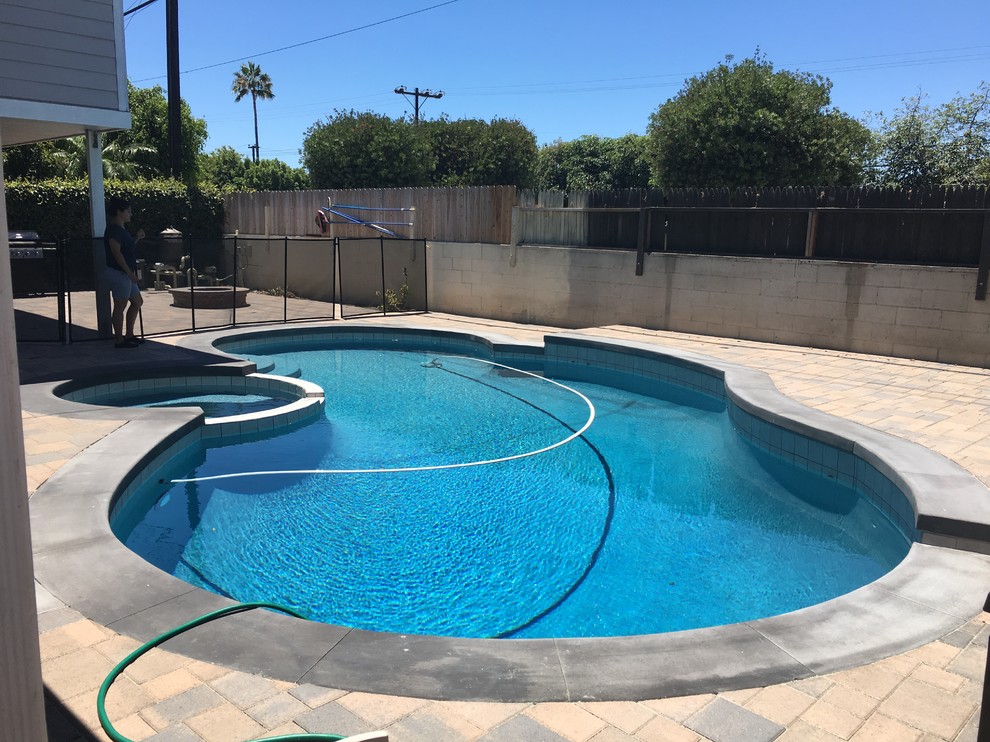 Photo of a mid-sized traditional backyard kidney-shaped lap pool in Orange County with a hot tub and natural stone pavers.