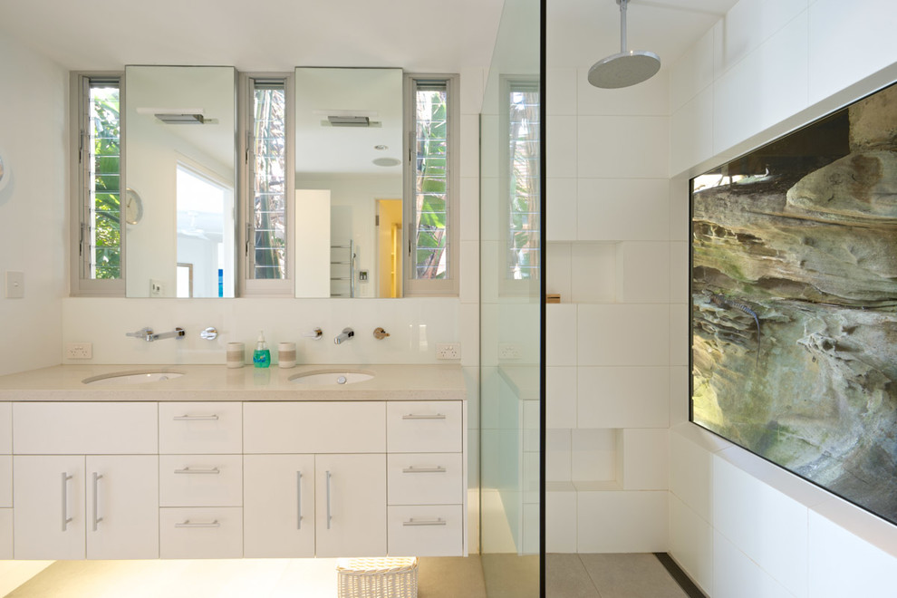 Photo of a mid-sized beach style bathroom in Sydney with white cabinets, white tile, ceramic tile, white walls, an undermount sink, engineered quartz benchtops, beige floor, an open shower, beige benchtops, flat-panel cabinets and a curbless shower.