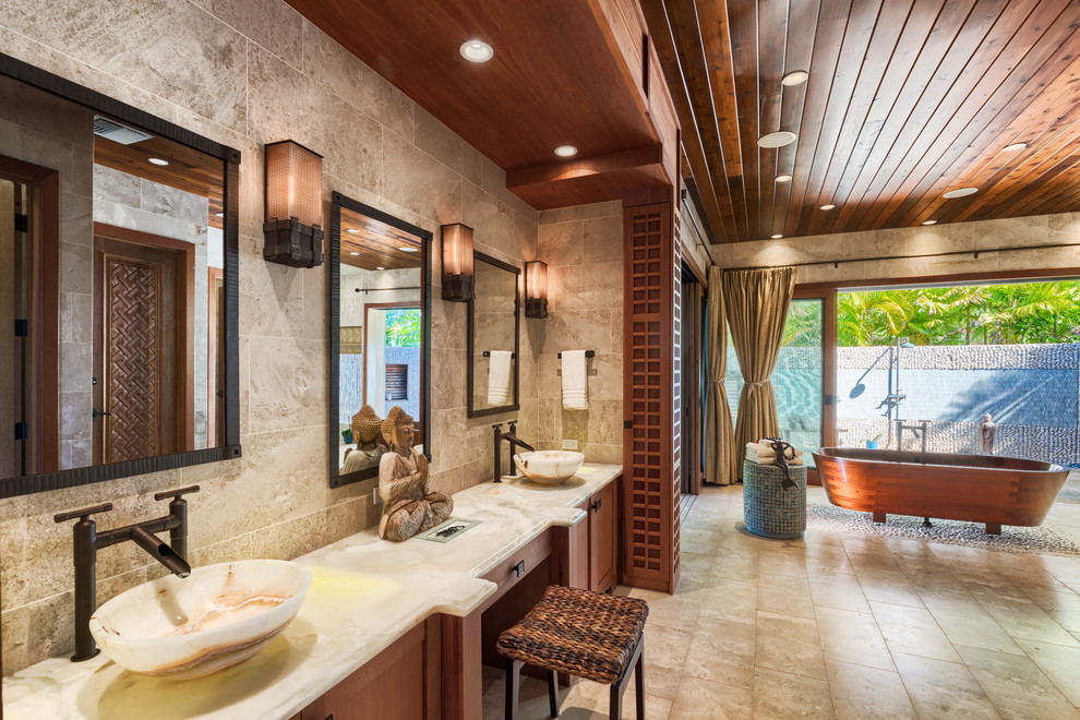 This is an example of a tropical master bathroom in Orange County with shaker cabinets, medium wood cabinets, a freestanding tub, beige tile, gray tile, beige walls, a vessel sink and beige floor.