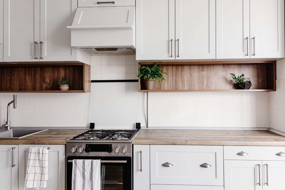 Eat-in kitchen - mid-sized transitional u-shaped dark wood floor and brown floor eat-in kitchen idea in DC Metro with a drop-in sink, recessed-panel cabinets, white cabinets, wood countertops, white backsplash, ceramic backsplash, stainless steel appliances, a peninsula and brown countertops