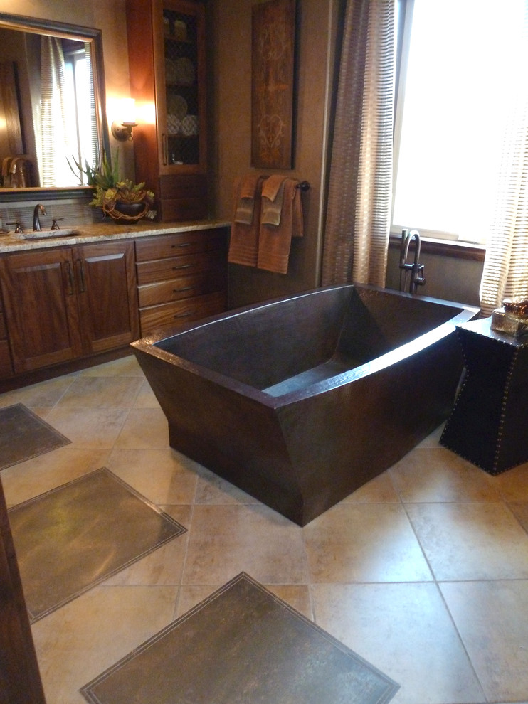 This is an example of a mid-sized mediterranean master bathroom in Denver with raised-panel cabinets, medium wood cabinets, a freestanding tub, beige walls, travertine floors, an undermount sink, granite benchtops, brown floor and brown benchtops.