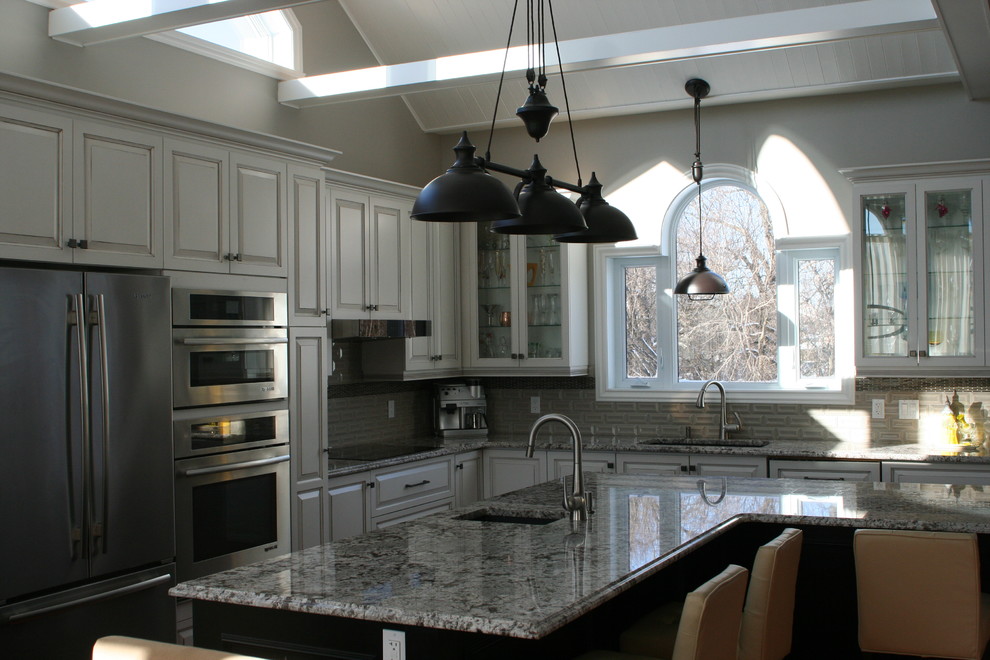 Example of a huge transitional l-shaped medium tone wood floor and brown floor open concept kitchen design in Montreal with an undermount sink, glass-front cabinets, white cabinets, granite countertops, gray backsplash, ceramic backsplash, stainless steel appliances, an island and multicolored countertops