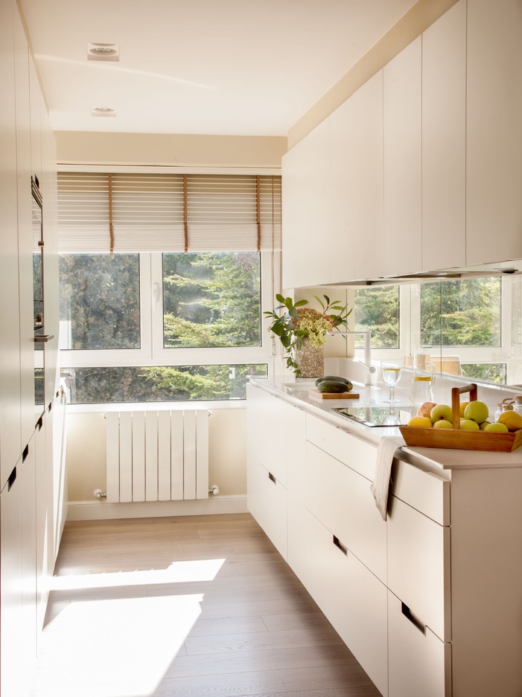 Photo of a mid-sized transitional single-wall kitchen in Bilbao with flat-panel cabinets, white cabinets, quartz benchtops, window splashback, stainless steel appliances, light hardwood floors, no island and beige floor.