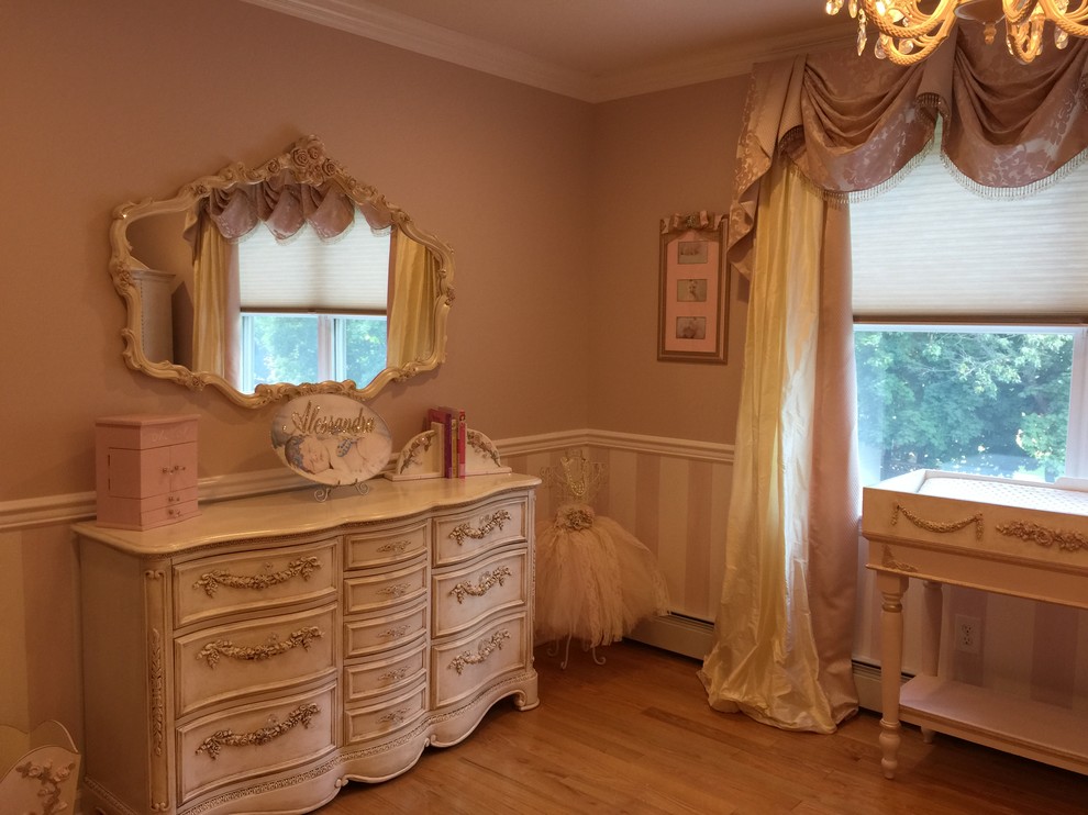 Photo of a large traditional nursery for girls in New York with pink walls and light hardwood floors.