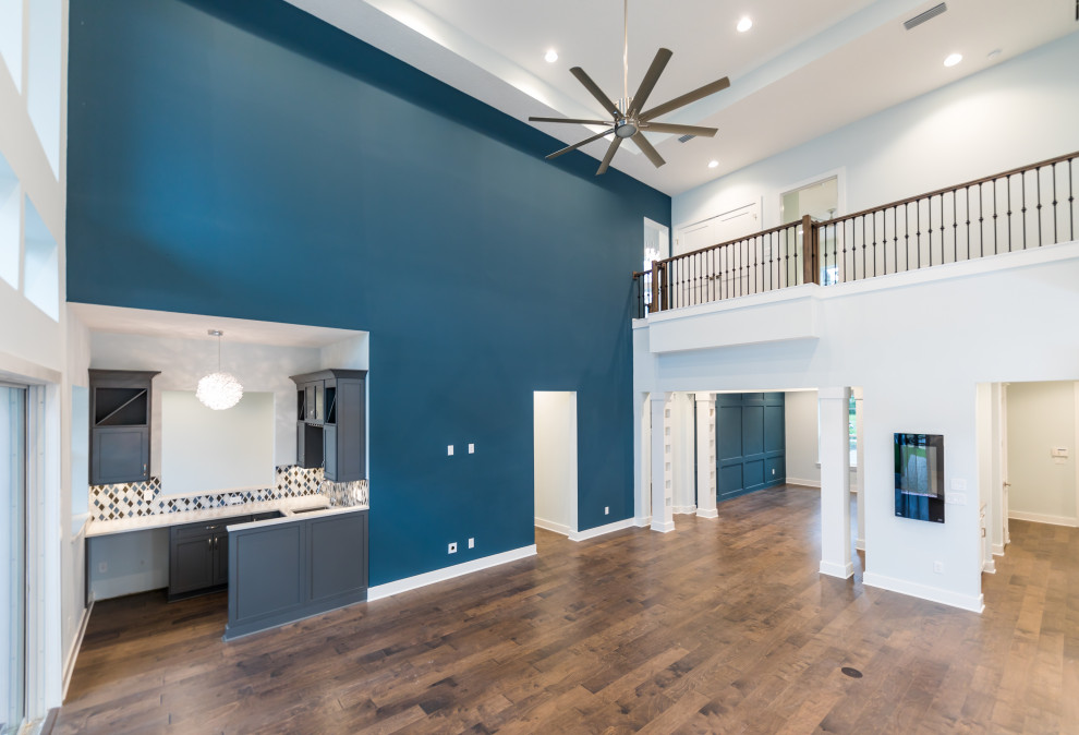 Expansive mediterranean open concept family room in Jacksonville with a home bar, blue walls, medium hardwood floors, a hanging fireplace, a wall-mounted tv and brown floor.
