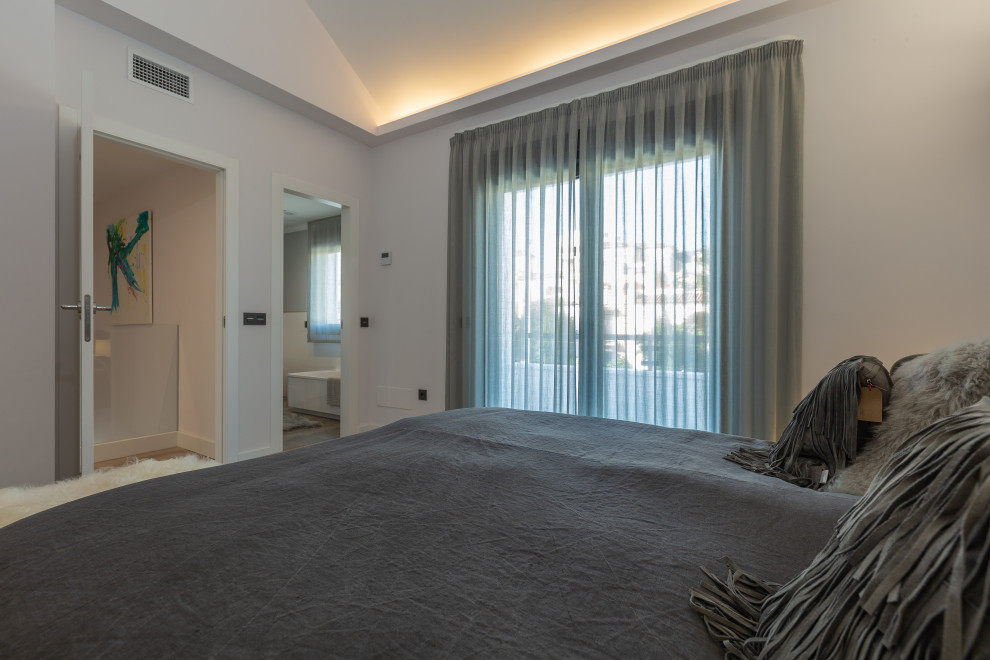 Immagine di una camera matrimoniale design di medie dimensioni con pareti bianche, pavimento in laminato e pavimento marrone