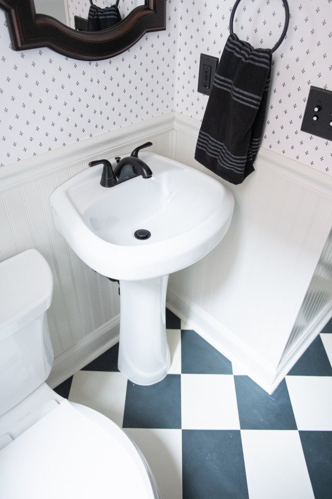 Inspiration for a powder room in Jacksonville with a one-piece toilet, grey walls, vinyl floors, a pedestal sink, black floor, a freestanding vanity and decorative wall panelling.
