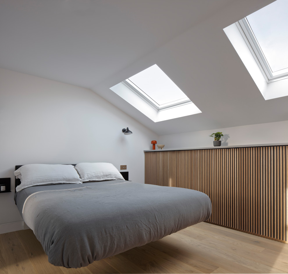 Medium sized contemporary master bedroom in London with white walls, light hardwood flooring, no fireplace and brown floors.