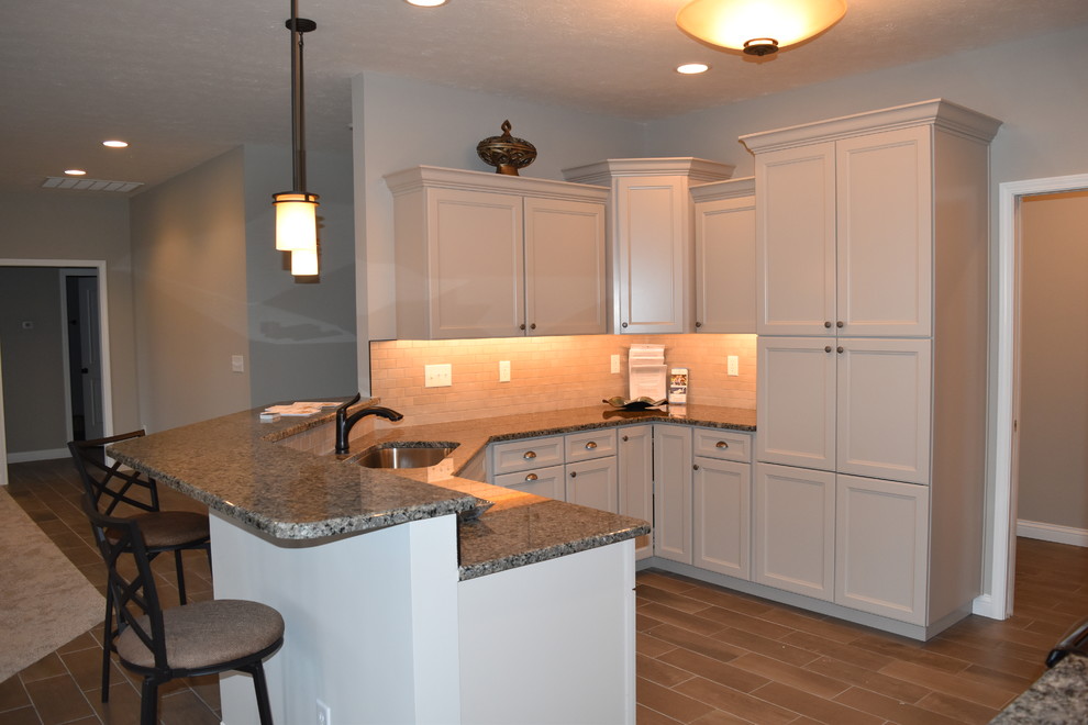Enclosed kitchen - mid-sized transitional u-shaped porcelain tile enclosed kitchen idea with an undermount sink, recessed-panel cabinets, beige cabinets, granite countertops, beige backsplash, subway tile backsplash and a peninsula