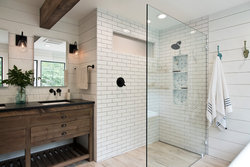 This is an example of a mid-sized country master bathroom in New York with dark wood cabinets, a freestanding tub, a curbless shower, white tile, subway tile, white walls, light hardwood floors, an undermount sink, beige floor, an open shower, black benchtops and flat-panel cabinets.