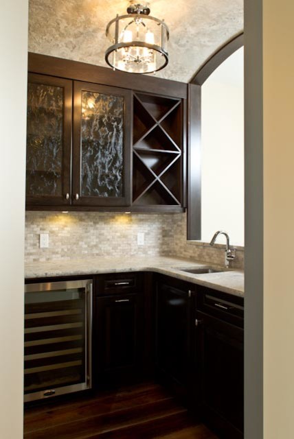 This is an example of a mid-sized transitional l-shaped wet bar in Calgary with an undermount sink, glass-front cabinets, dark wood cabinets, soapstone benchtops, grey splashback, mosaic tile splashback, dark hardwood floors and brown floor.