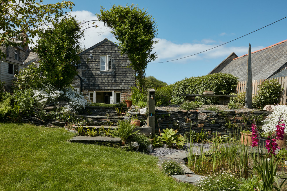 Foto di un giardino tradizionale esposto in pieno sole dietro casa in estate con pavimentazioni in pietra naturale e recinzione in pietra