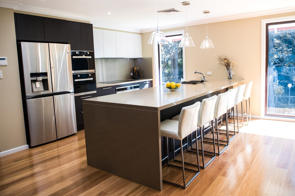Photo of a mid-sized contemporary galley eat-in kitchen in Sydney with a double-bowl sink, flat-panel cabinets, brown cabinets, quartz benchtops, beige splashback, glass sheet splashback, stainless steel appliances, medium hardwood floors and with island.