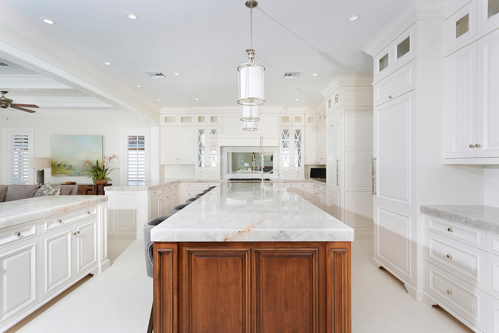 This is an example of an expansive beach style u-shaped open plan kitchen in Miami with white cabinets, quartzite benchtops, limestone floors, multiple islands, white floor, raised-panel cabinets, panelled appliances and white benchtop.