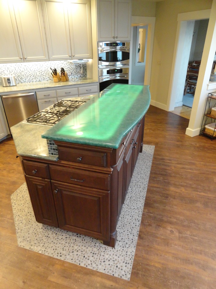 This is an example of a large beach style l-shaped eat-in kitchen in Seattle with an undermount sink, distressed cabinets, green splashback, stainless steel appliances, glass sheet splashback, dark hardwood floors and with island.