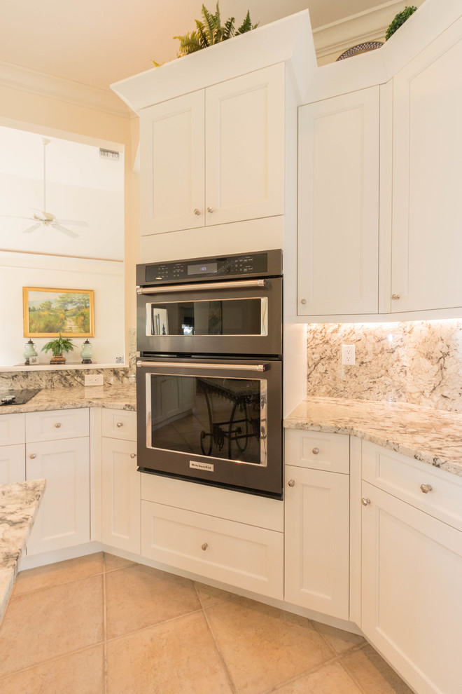 Inspiration for a large transitional porcelain tile eat-in kitchen remodel in Miami with an undermount sink, shaker cabinets, white cabinets, granite countertops, gray backsplash, stone slab backsplash, black appliances and an island