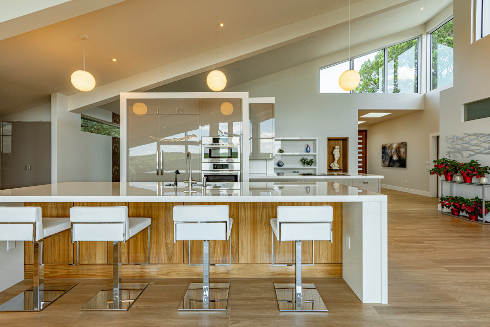 This is an example of a large midcentury galley open plan kitchen in Austin with an undermount sink, flat-panel cabinets, grey cabinets, quartz benchtops, white splashback, stainless steel appliances, light hardwood floors, multiple islands, beige floor and white benchtop.