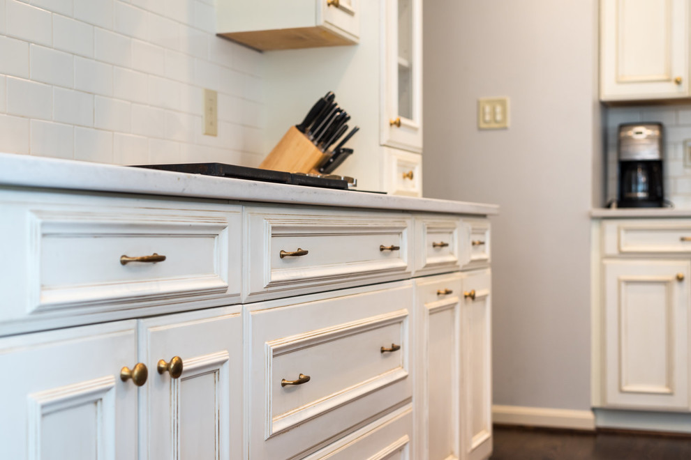Example of a transitional medium tone wood floor and brown floor kitchen design in DC Metro with an undermount sink, recessed-panel cabinets, white cabinets, granite countertops, white backsplash, subway tile backsplash, stainless steel appliances, an island and white countertops