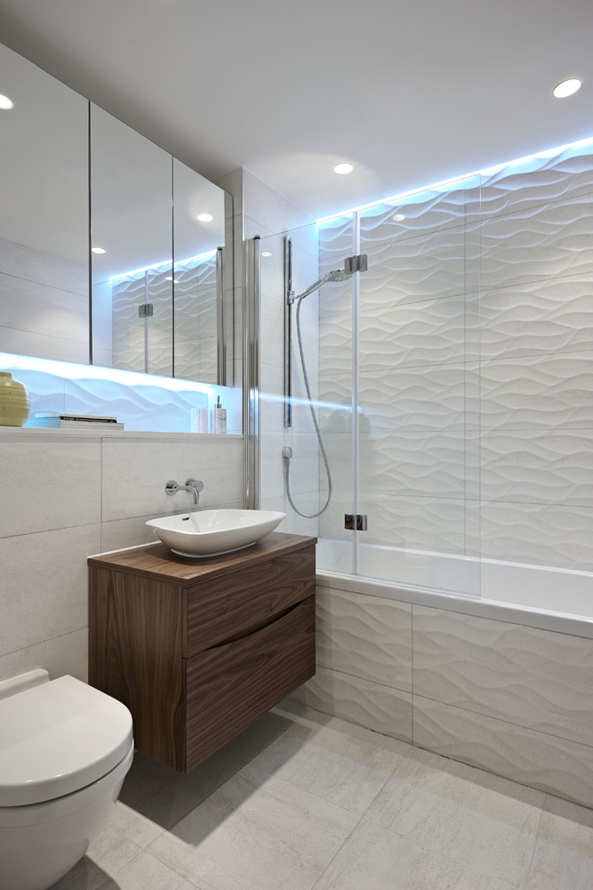 Photo of a contemporary bathroom in London with a vessel sink, flat-panel cabinets, dark wood cabinets, wood benchtops, a drop-in tub, a shower/bathtub combo, a wall-mount toilet, white tile and brown benchtops.