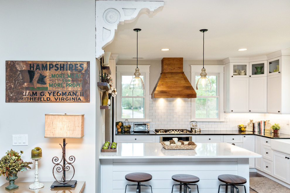 Photo of a country kitchen in Other with a farmhouse sink, shaker cabinets, white cabinets, white splashback, subway tile splashback, dark hardwood floors, a peninsula and brown floor.