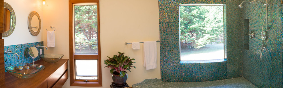 This is an example of a mid-sized eclectic master bathroom in Other with flat-panel cabinets, medium wood cabinets, a corner shower, a two-piece toilet, blue tile, glass tile, beige walls, porcelain floors, a vessel sink and wood benchtops.