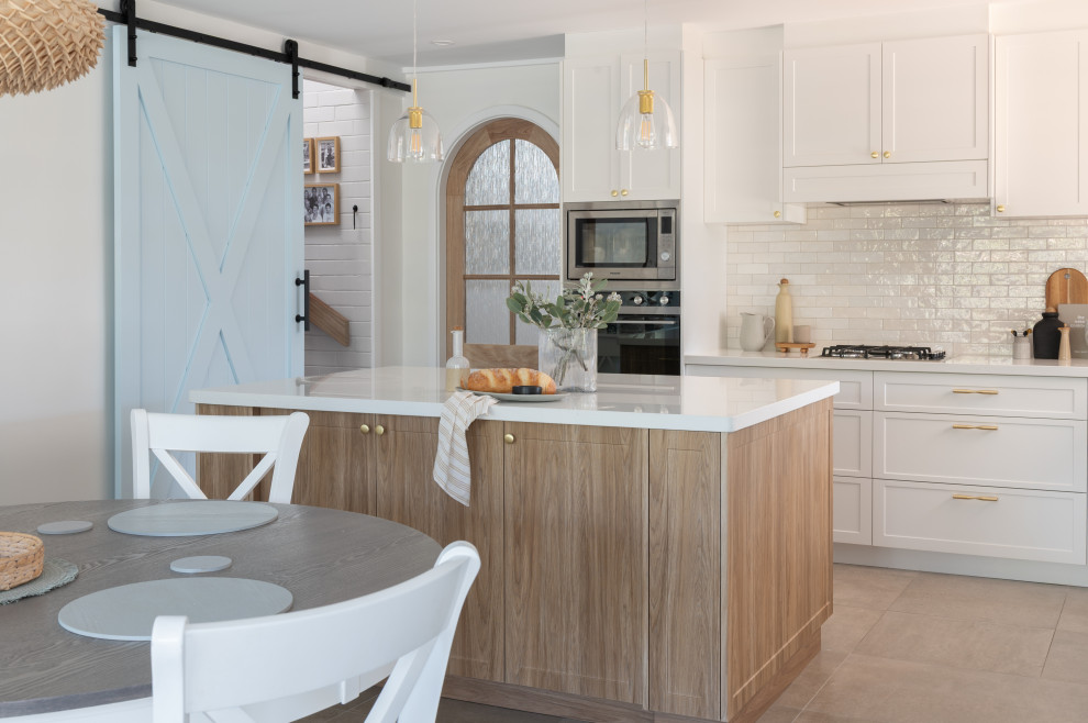 Photo of a beach style eat-in kitchen in Perth with shaker cabinets, white cabinets, solid surface benchtops, white splashback, ceramic splashback, with island and white benchtop.