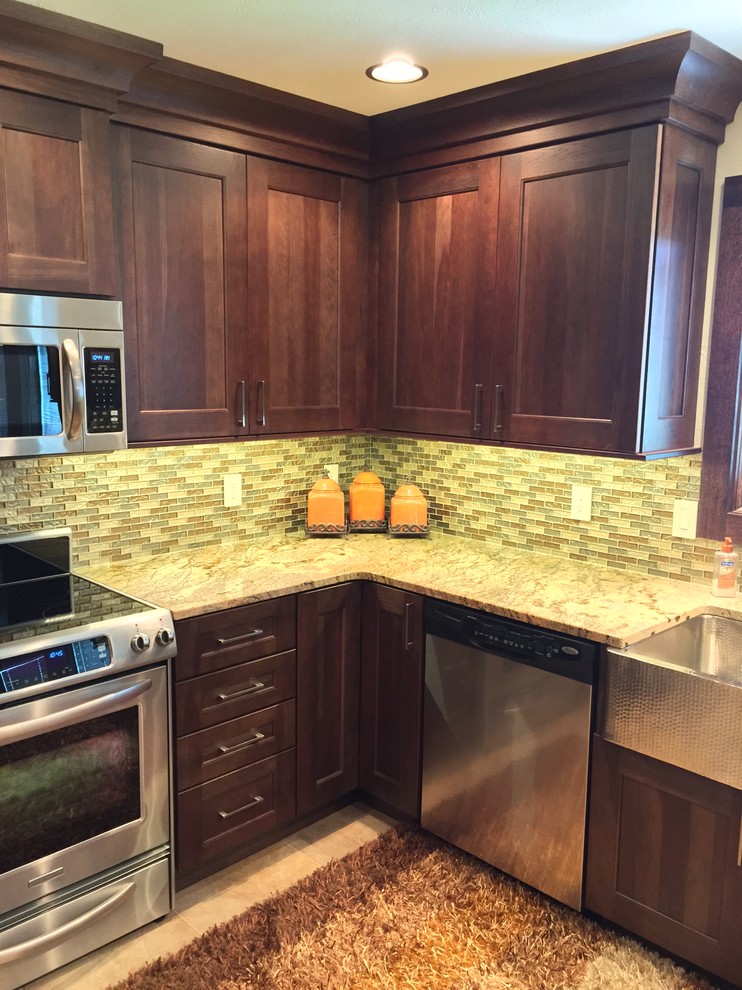 This is an example of a mid-sized transitional u-shaped eat-in kitchen in Omaha with a farmhouse sink, dark wood cabinets, granite benchtops, glass tile splashback, stainless steel appliances, porcelain floors, a peninsula, shaker cabinets, brown splashback and beige floor.