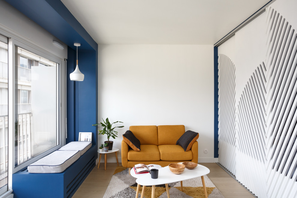Minimalistisk inredning av ett litet allrum med öppen planlösning, med ett bibliotek, blå väggar, laminatgolv, en dold TV och brunt golv