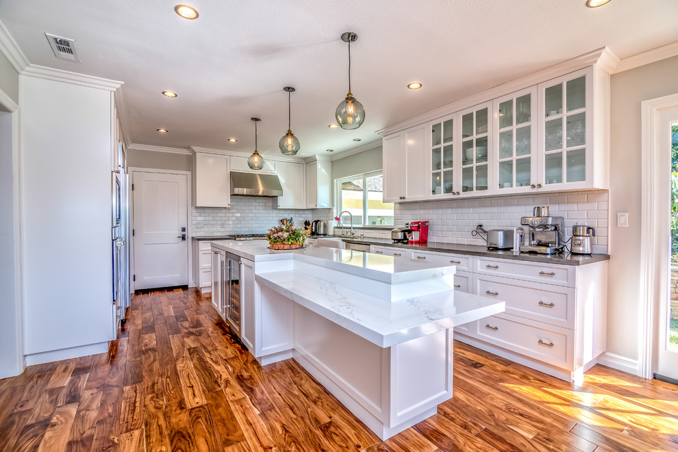 Photo of a large traditional u-shaped eat-in kitchen in San Francisco with shaker cabinets, white cabinets, marble benchtops, white splashback, subway tile splashback, stainless steel appliances, medium hardwood floors, with island and grey benchtop.
