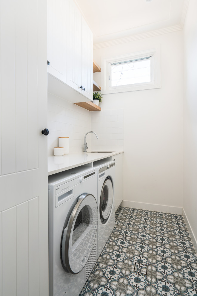 Photo of a beach style galley dedicated laundry room in Sydney with a single-bowl sink, shaker cabinets, white cabinets, quartz benchtops, white splashback, subway tile splashback, white walls, porcelain floors, a side-by-side washer and dryer and white benchtop.