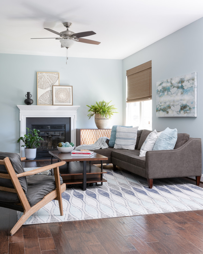 This is an example of a beach style family room in DC Metro with blue walls, medium hardwood floors, a standard fireplace, a wood fireplace surround, a freestanding tv and brown floor.