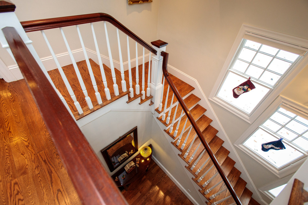 Large traditional wood u-shaped staircase in Boston with painted wood risers and wood railing.