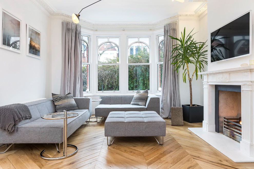 Photo of a transitional living room in London with white walls, medium hardwood floors, a standard fireplace, a wall-mounted tv and brown floor.