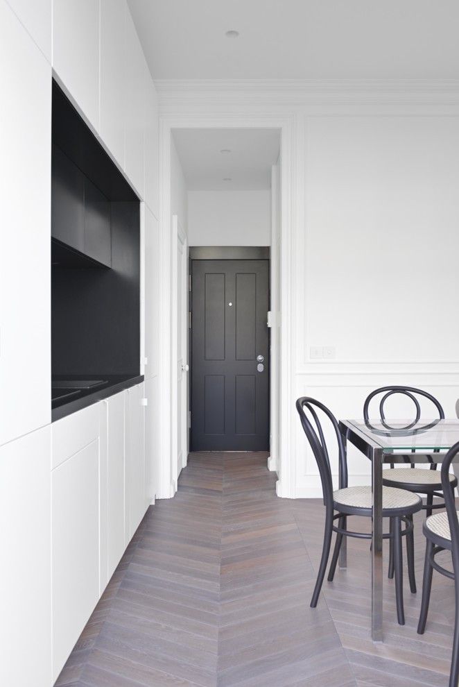 Design ideas for a small traditional single-wall open plan kitchen in London with a drop-in sink, recessed-panel cabinets, white cabinets, wood benchtops, black splashback, black appliances, light hardwood floors, no island, brown floor and black benchtop.