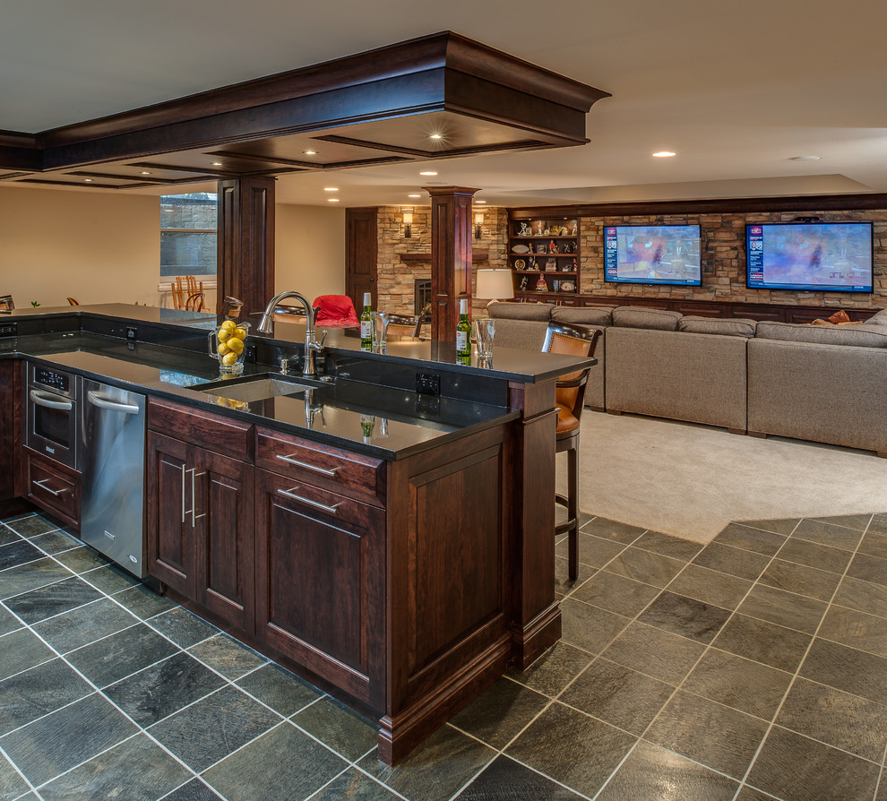 This is an example of a large transitional galley seated home bar in Detroit with an undermount sink, raised-panel cabinets, dark wood cabinets, granite benchtops and slate floors.