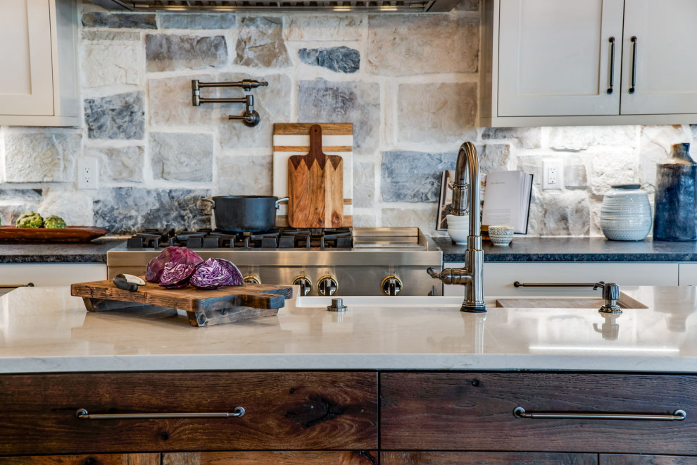 Photo of a large country u-shaped open plan kitchen in Denver with a farmhouse sink, recessed-panel cabinets, beige cabinets, quartz benchtops, beige splashback, stone tile splashback, stainless steel appliances, medium hardwood floors, with island, brown floor, white benchtop and wood.