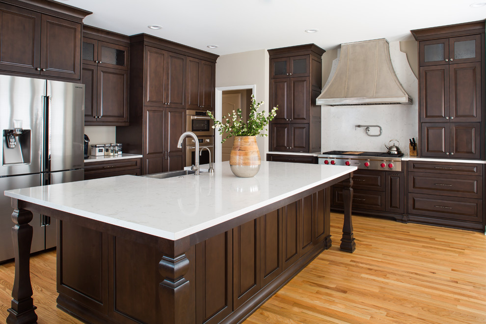 Example of a large transitional l-shaped light wood floor open concept kitchen design in Atlanta with a farmhouse sink, raised-panel cabinets, dark wood cabinets, quartz countertops, white backsplash, stone slab backsplash, stainless steel appliances and an island