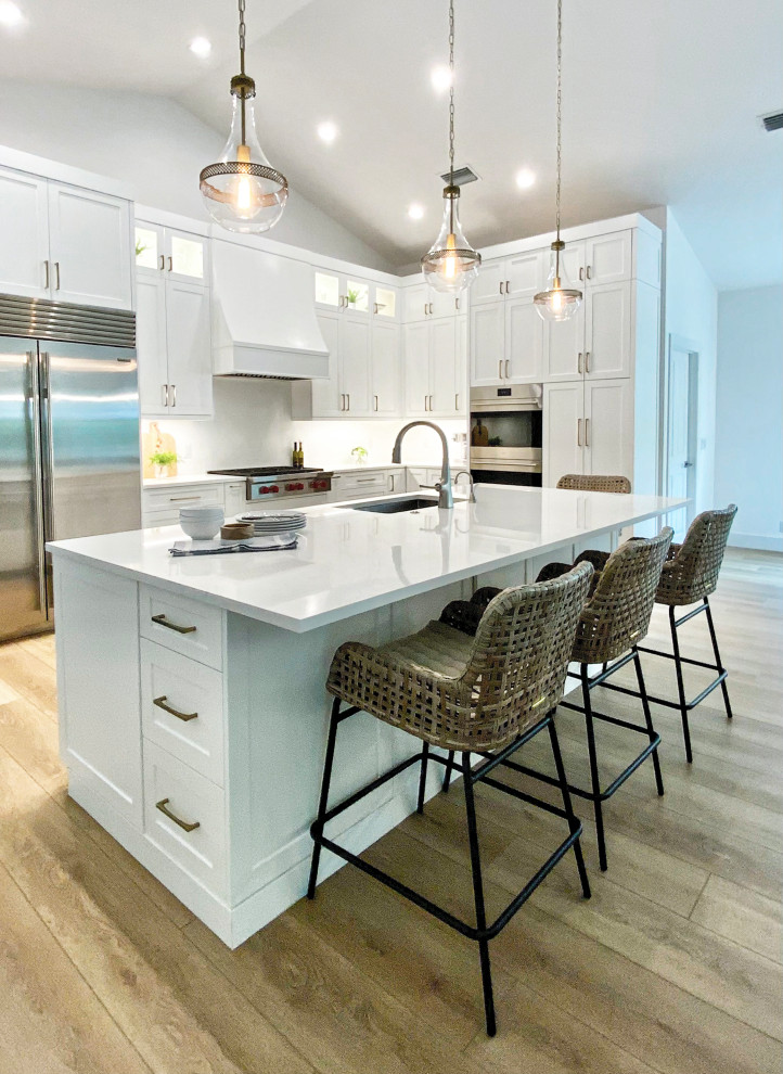Design ideas for a large beach style l-shaped open plan kitchen in Miami with an undermount sink, shaker cabinets, white cabinets, quartz benchtops, white splashback, engineered quartz splashback, stainless steel appliances, vinyl floors, with island, beige floor and white benchtop.