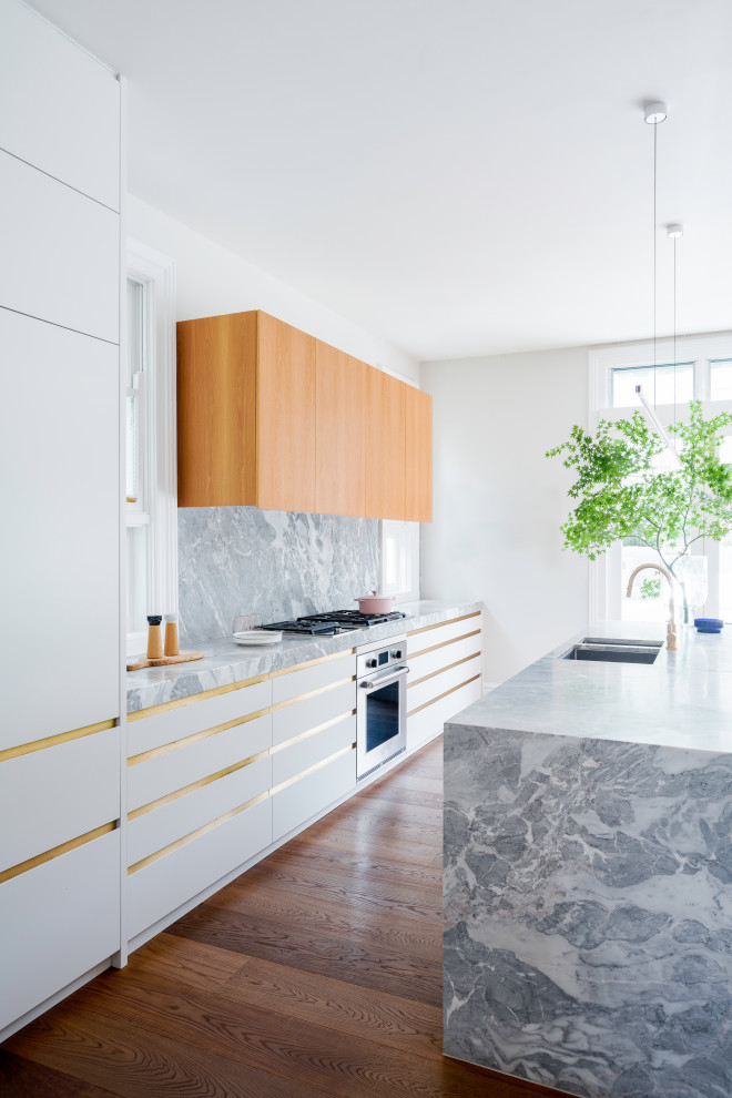 Große Moderne Wohnküche mit Unterbauwaschbecken, flächenbündigen Schrankfronten, Kalkstein-Arbeitsplatte, Küchenrückwand in Grau, braunem Holzboden, Kücheninsel und grauer Arbeitsplatte in Sydney