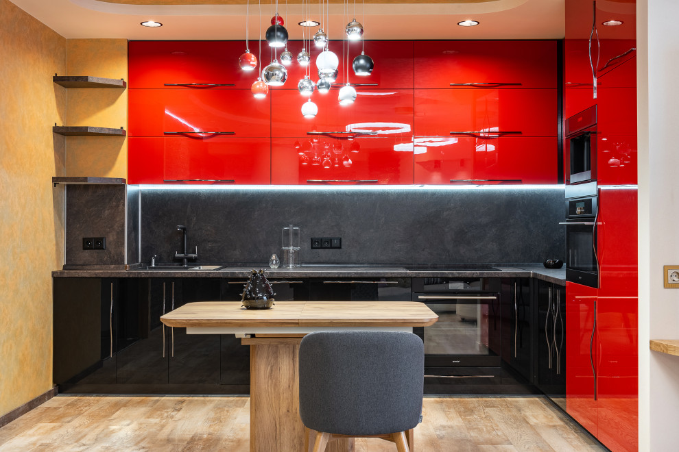 Contemporary l-shaped kitchen in Other with a drop-in sink, flat-panel cabinets, red cabinets, black splashback, black appliances, with island, beige floor and black benchtop.