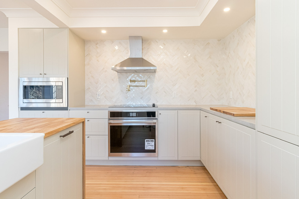 Eat-in kitchen - mid-sized transitional l-shaped light wood floor, brown floor and coffered ceiling eat-in kitchen idea with a farmhouse sink, beaded inset cabinets, beige cabinets, quartzite countertops, beige backsplash, ceramic backsplash, stainless steel appliances, an island and gray countertops