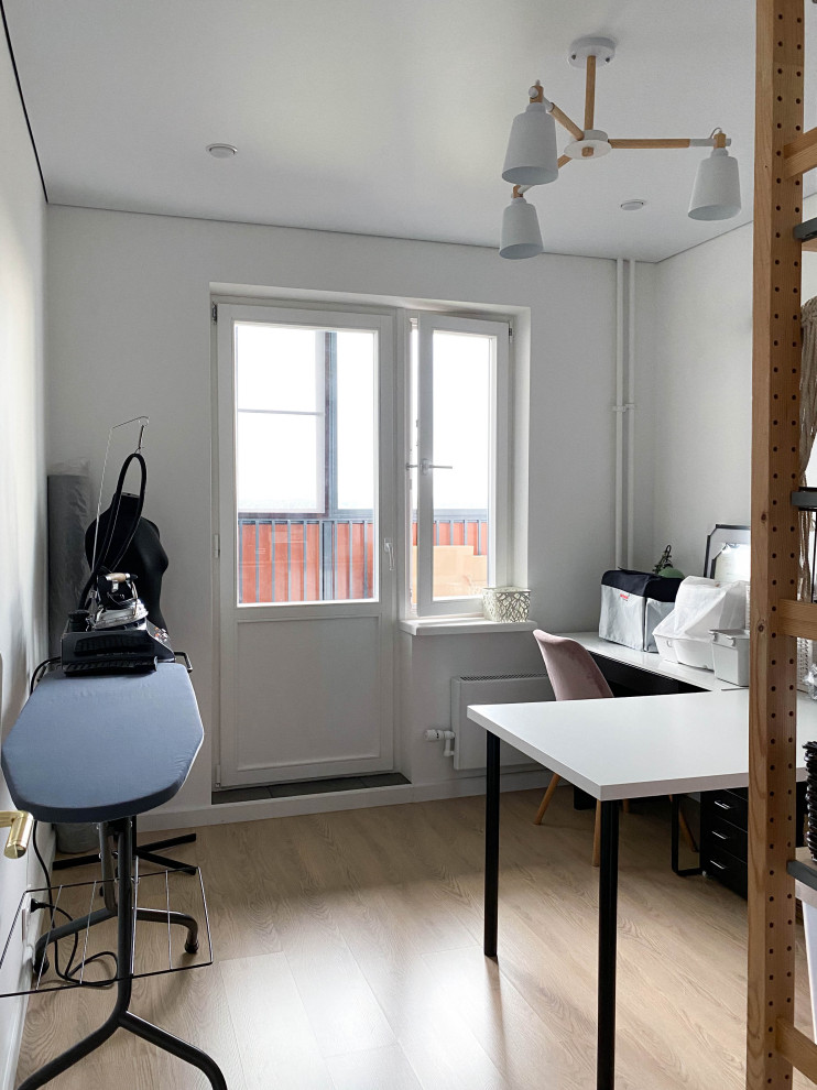 Foto på ett litet skandinaviskt hobbyrum, med vita väggar, laminatgolv och ett fristående skrivbord
