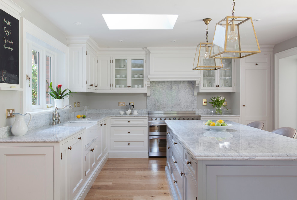 Transitional l-shaped kitchen in Dublin with a farmhouse sink, recessed-panel cabinets, white cabinets, marble benchtops, stainless steel appliances, light hardwood floors and with island.