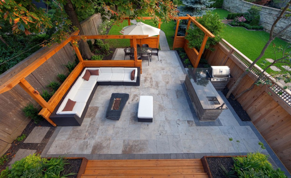 This is an example of a contemporary backyard patio in Toronto with an outdoor kitchen, natural stone pavers and no cover.
