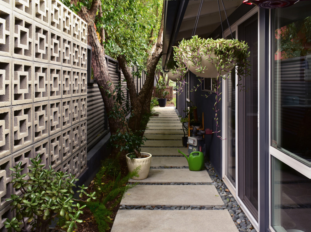 Photo of a mid-sized midcentury front yard partial sun driveway for winter in Los Angeles with a garden path, concrete pavers and a metal fence.