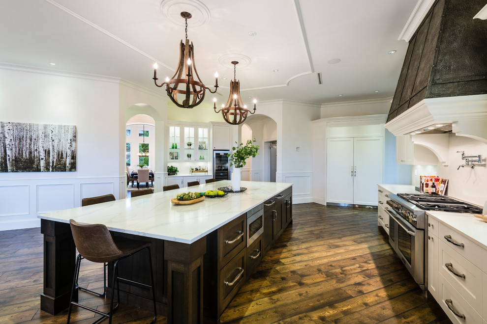 Inspiration for a huge rustic u-shaped medium tone wood floor and brown floor open concept kitchen remodel in Vancouver with an undermount sink, shaker cabinets, white cabinets, solid surface countertops, white backsplash, stone slab backsplash, stainless steel appliances, an island and white countertops