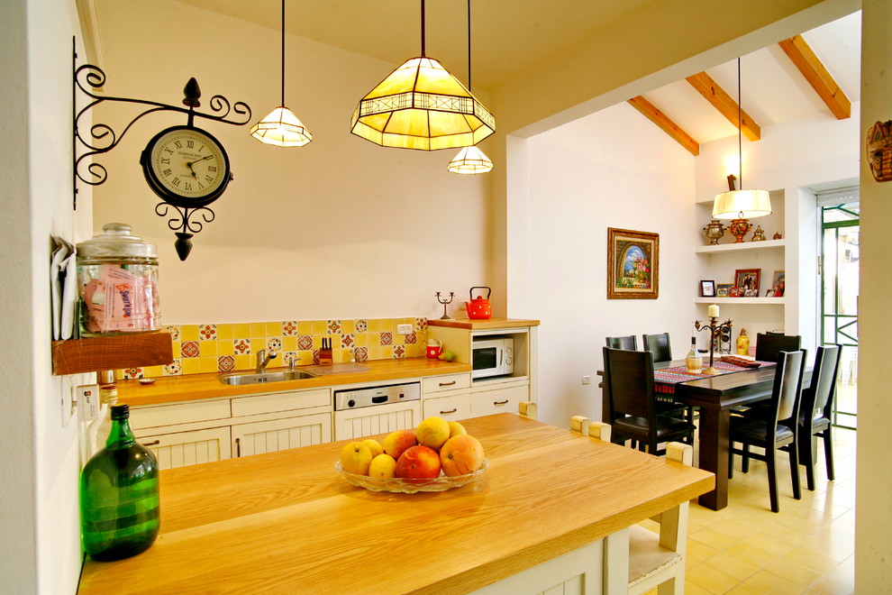 Photo of a mediterranean eat-in kitchen in Tel Aviv with wood benchtops, multi-coloured splashback, panelled appliances, a drop-in sink and white cabinets.