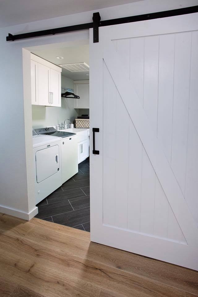 Design ideas for a mid-sized country utility room in San Francisco with an utility sink, shaker cabinets, white cabinets, white walls, ceramic floors, a side-by-side washer and dryer and black floor.