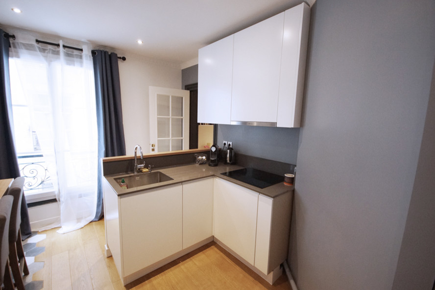 This is an example of a mid-sized contemporary galley open plan kitchen in Paris with light hardwood floors, an undermount sink, beaded inset cabinets, white cabinets, wood benchtops, grey splashback, stone slab splashback, panelled appliances and with island.